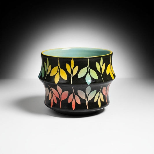 CeramicMeltdown.com rainbow leaf cocktail cup with a light blue interior and a black exterior adorned with colorful gradient leaves.