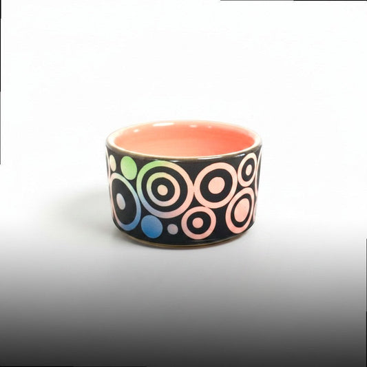 CeramicMeltdown.com handcrafted ceramic trinket dish with concentric circles in rainbow gradient on black, coral interior.