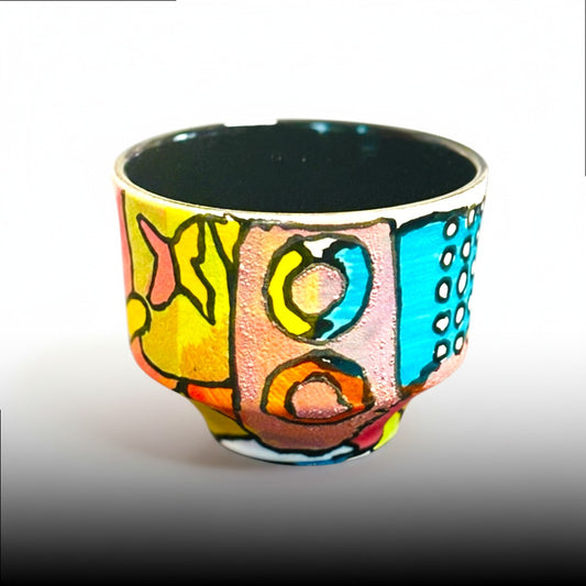CeramicMeltdown.com hand-painted ceramic cup with abstract colorful design, featuring yellow, pink, blue, and orange geometric shapes and dots.