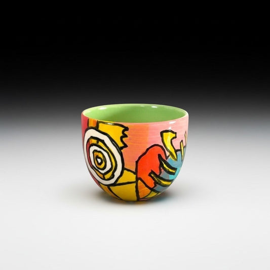 CeramicMeltdown.com abstract art wine cup with a green interior and a vibrant, multi-colored exterior featuring bold black lines and shapes.