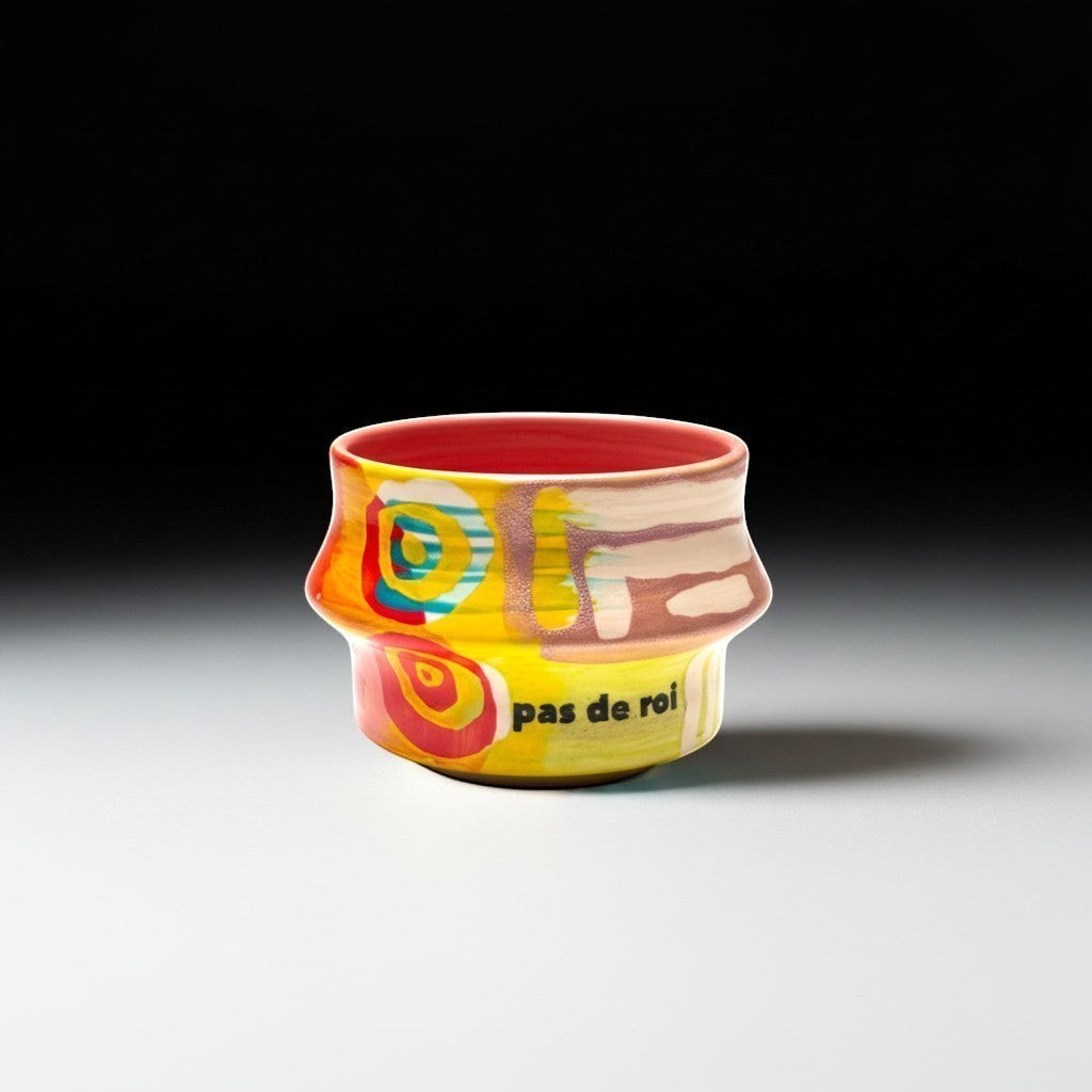 CeramicMeltdown.com Freedom Cup, a small, brightly painted ceramic vessel with a coral pink interior and abstract yellow, red, blue, and white designs. Text reads "pas de roi".