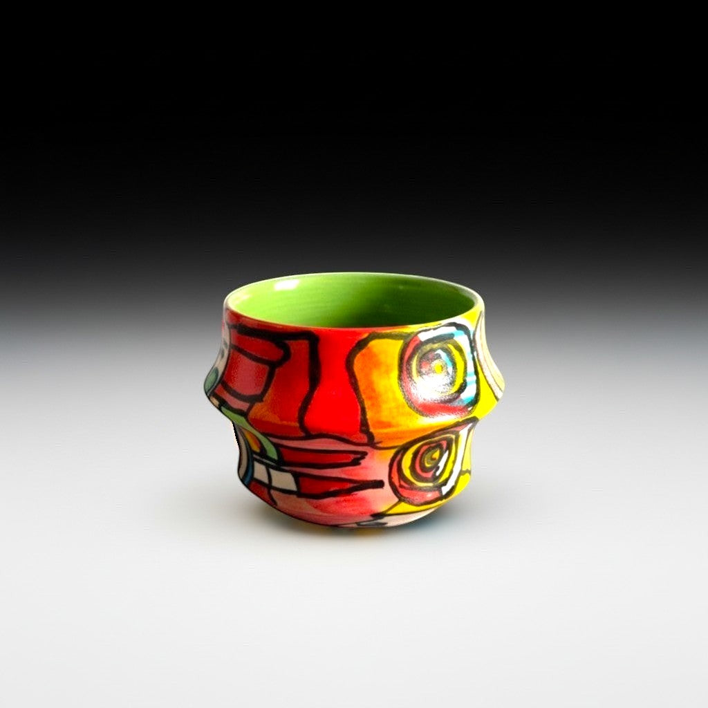 CeramicMeltdown.com Freedom Cup, a vibrant, hand-painted ceramic vessel with a green interior and a bold, abstract design in red, yellow, and black.